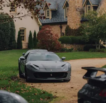 Aerial view of a small village with red-tiled roofs, surrounded by autumn foliage and fields, under a bright blue sky.