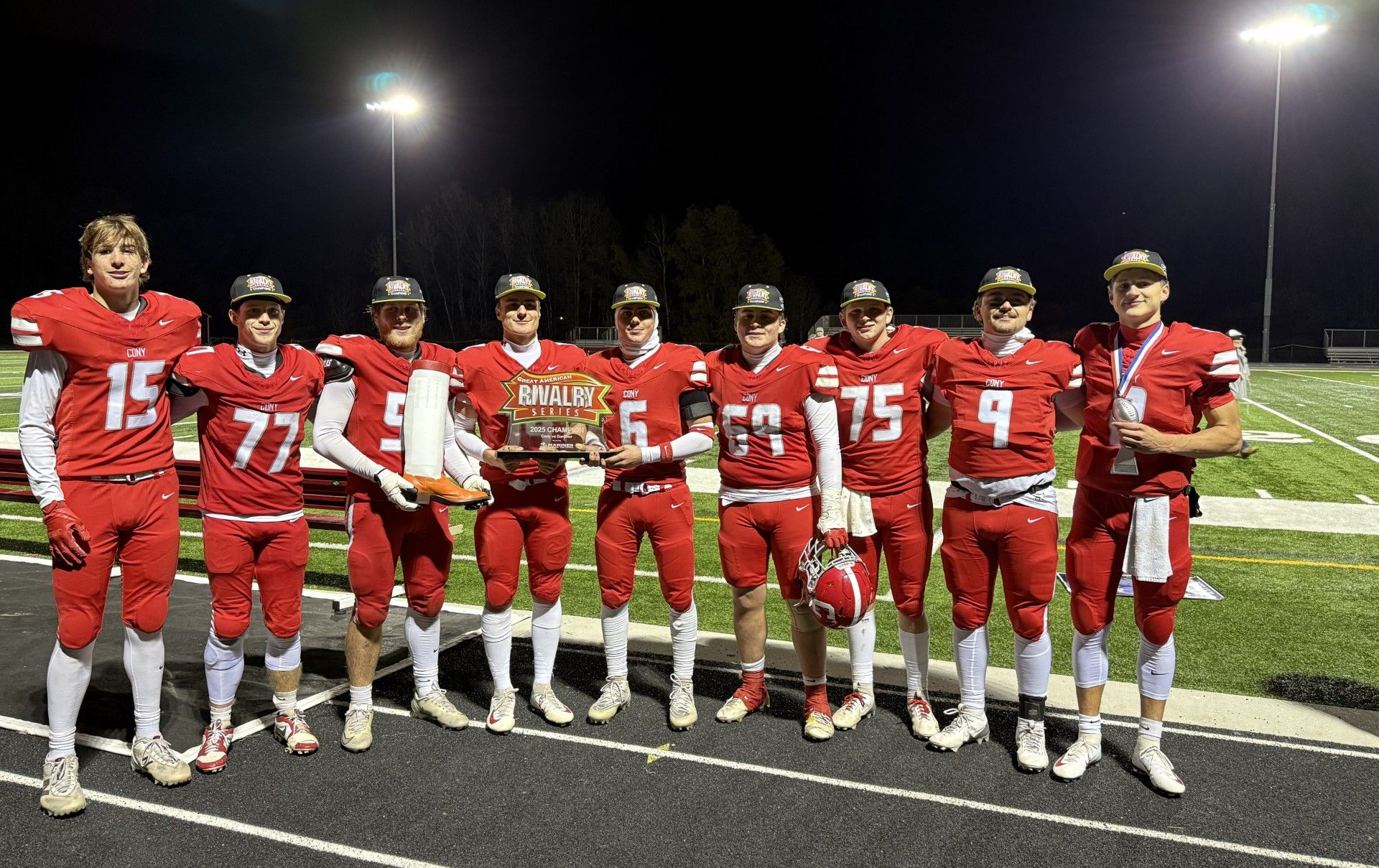Football team in red uniforms holding a trophy on a field at night.