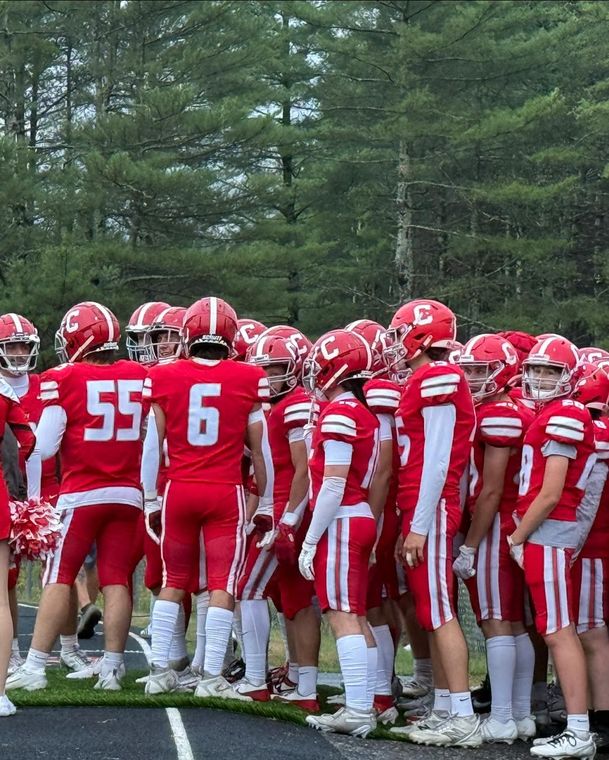 Football team huddle in red and white uniforms. Players facing each other on a green field.