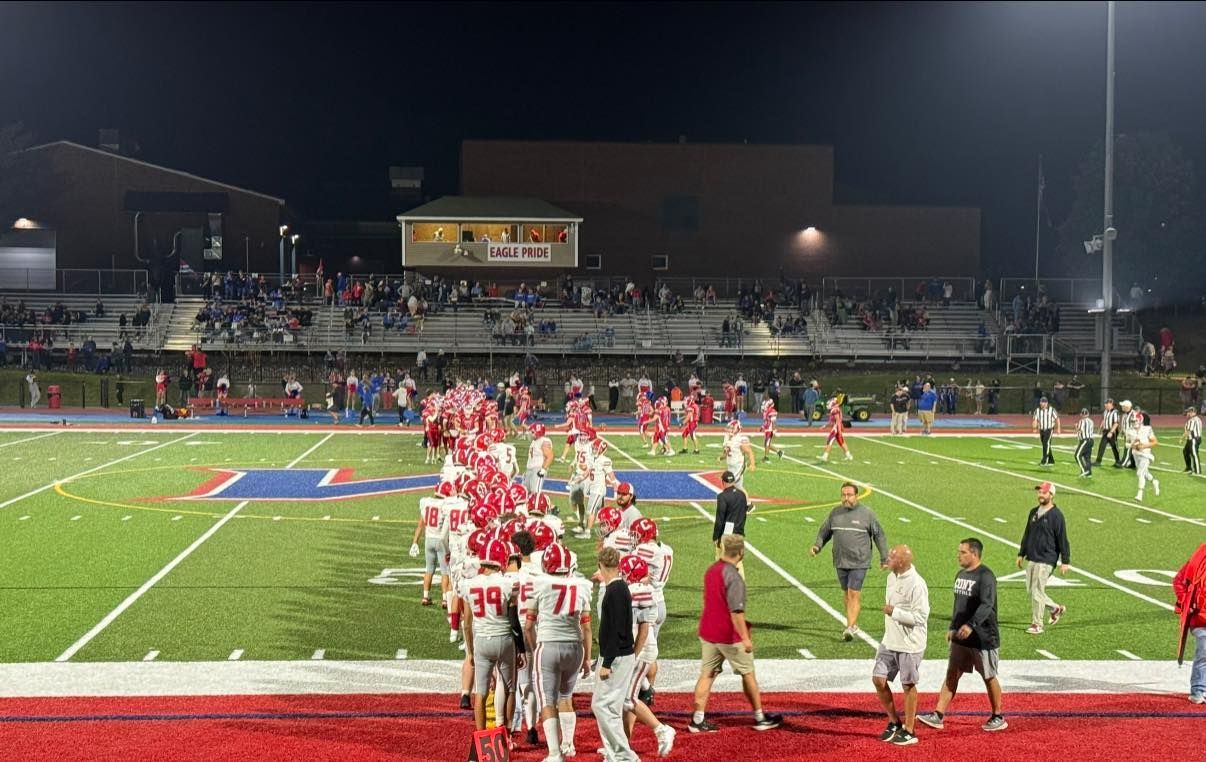 Football team in red uniforms on a field with spectators in the stands at night.