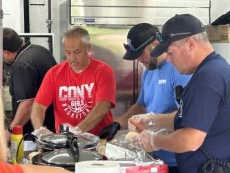 People preparing food in a kitchen: man in red shirt, blue shirt, black hat, another in dark blue.