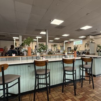 Quiet diner interior with wooden bar stools, light blue counter, and ceiling lights.