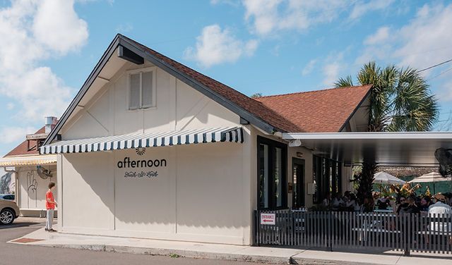 Street-corner café with white façade, striped awning, and outdoor seating under a red roof.