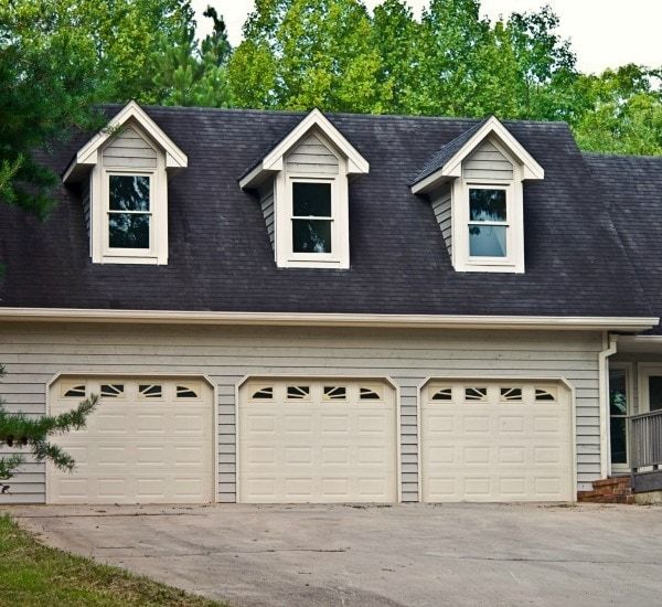 A house with three garage doors and a black roof