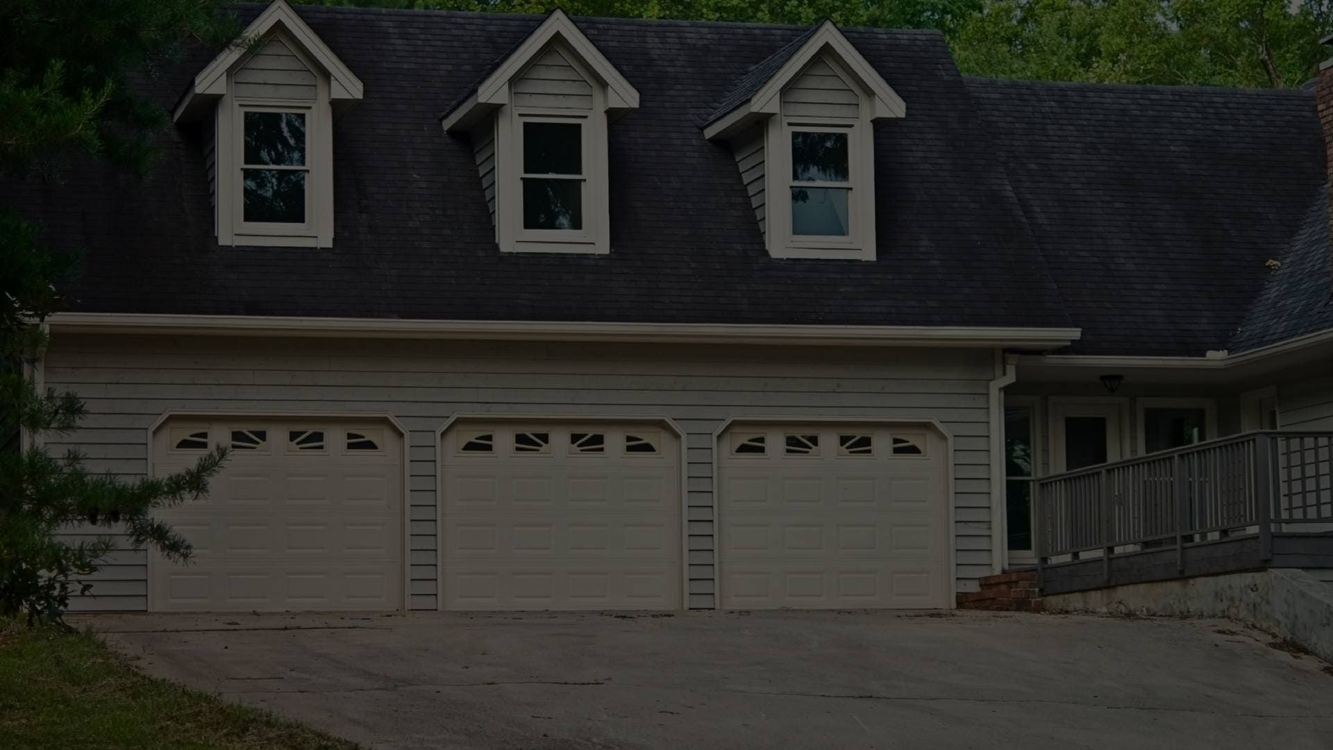 A large white house with three garage doors and a black roof.
