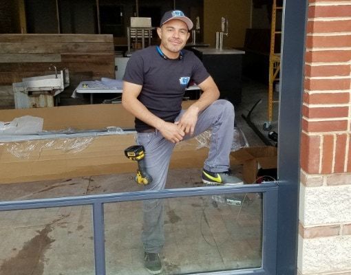 a man is kneeling on a window sill holding a drill