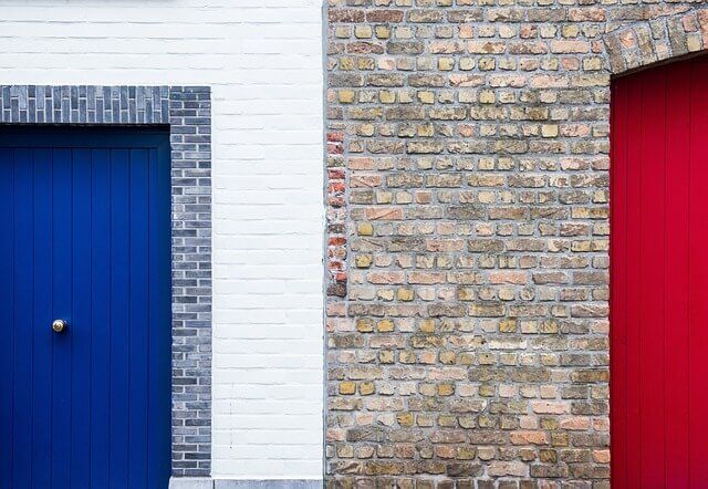 A blue door and a red door are next to each other on a brick wall.
