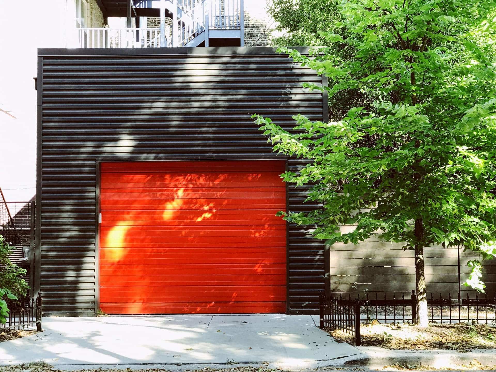 A red garage door is sitting in front of a black building.