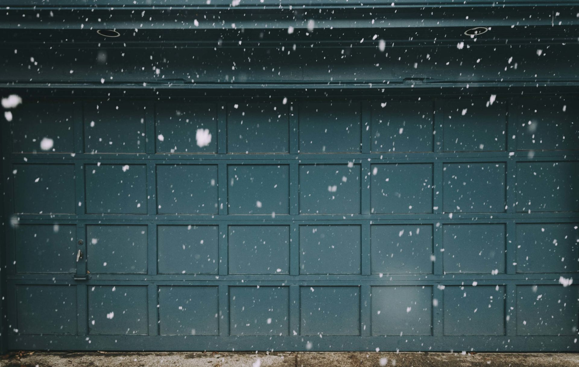It is snowing outside of a garage door.