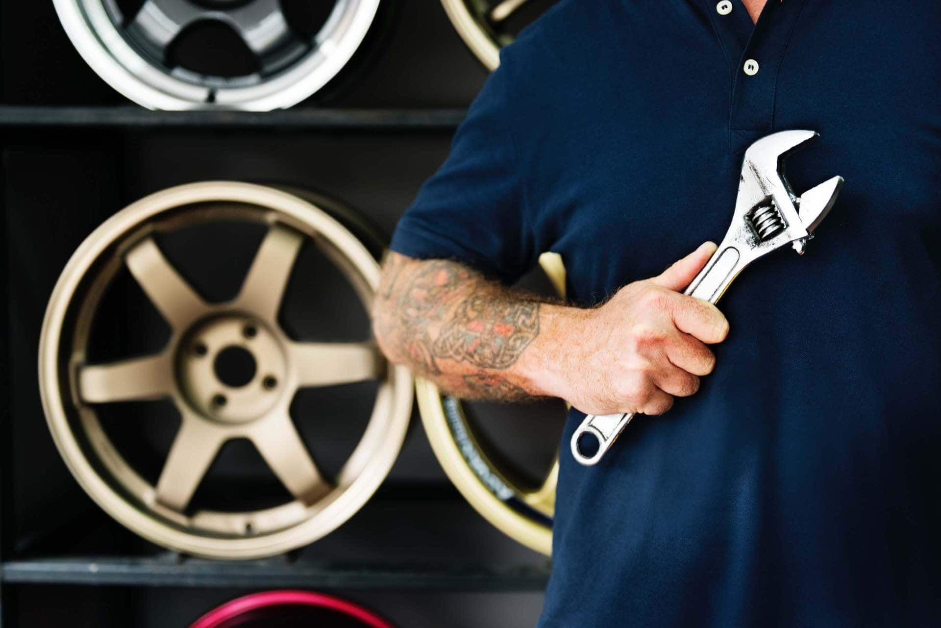 A man is holding a wrench in front of a display of wheels.