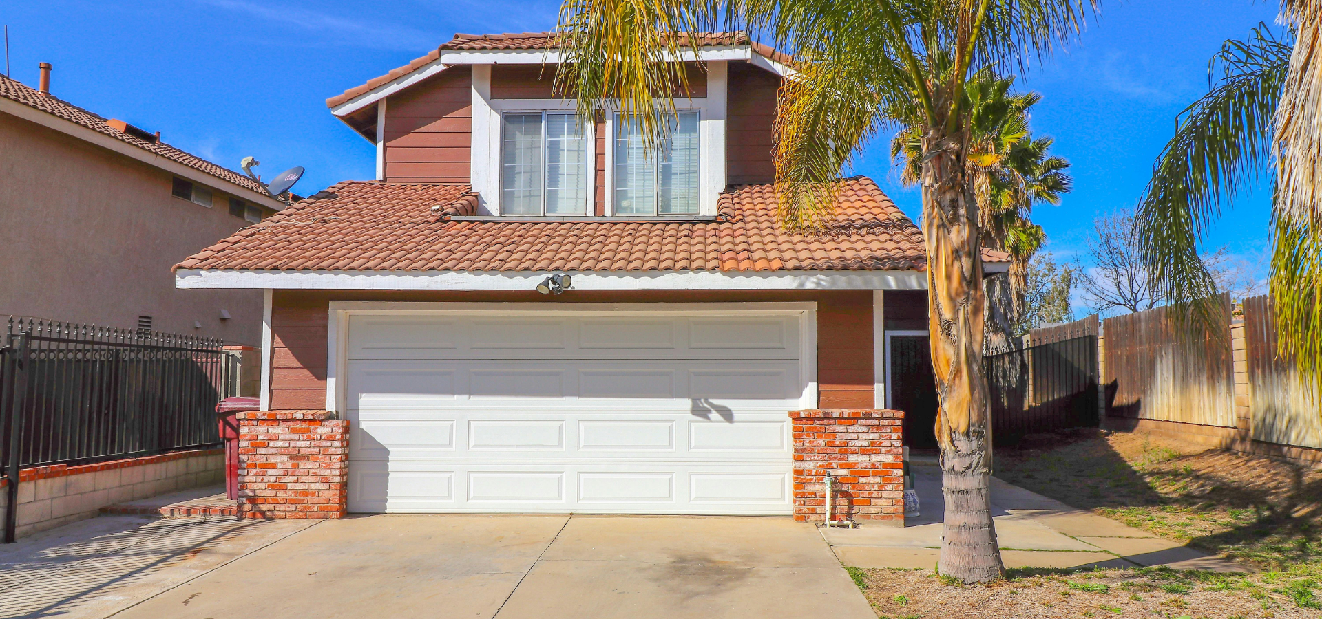 Suburban house with a red tile roof, white garage door, and palm tree in the front yard
