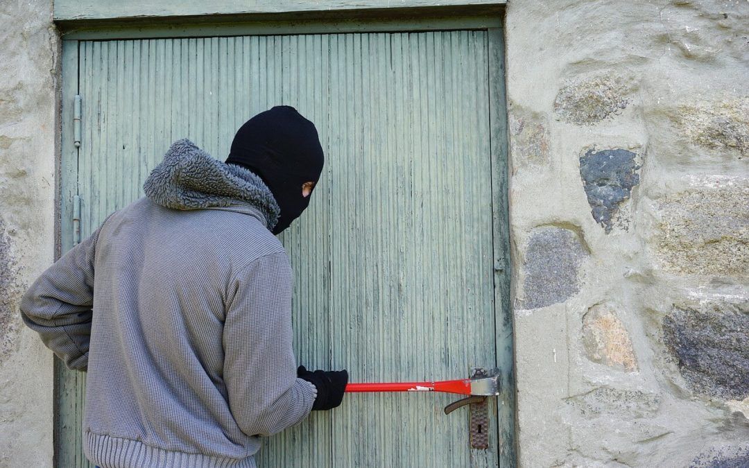 A man in a mask is trying to open a door with a hammer.