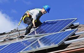 A man is installing solar panels on the roof of a house.