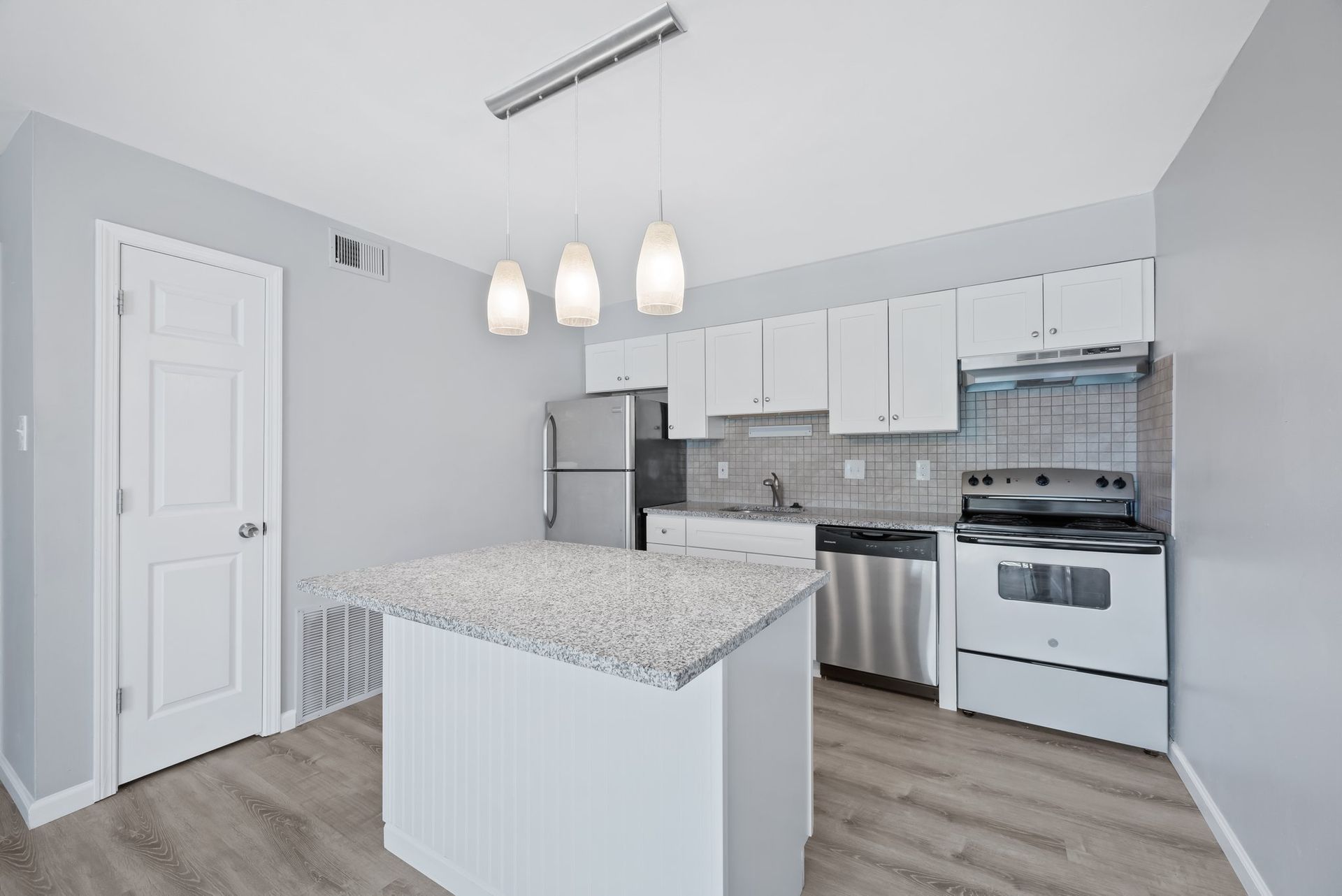A kitchen with white cabinets , stainless steel appliances , and a large island.