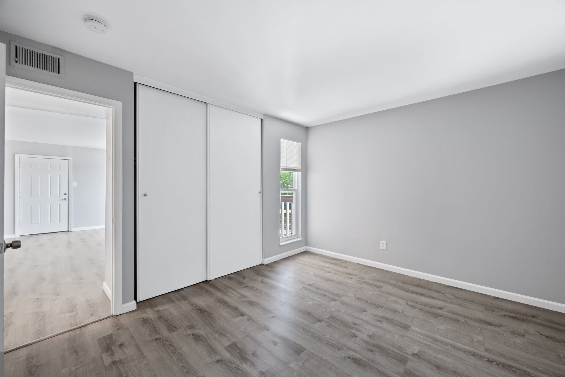 An empty bedroom with hardwood floors and white walls.
