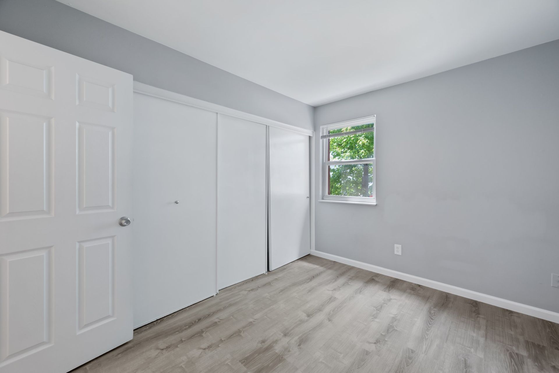 An empty bedroom with hardwood floors , white doors , and a window.