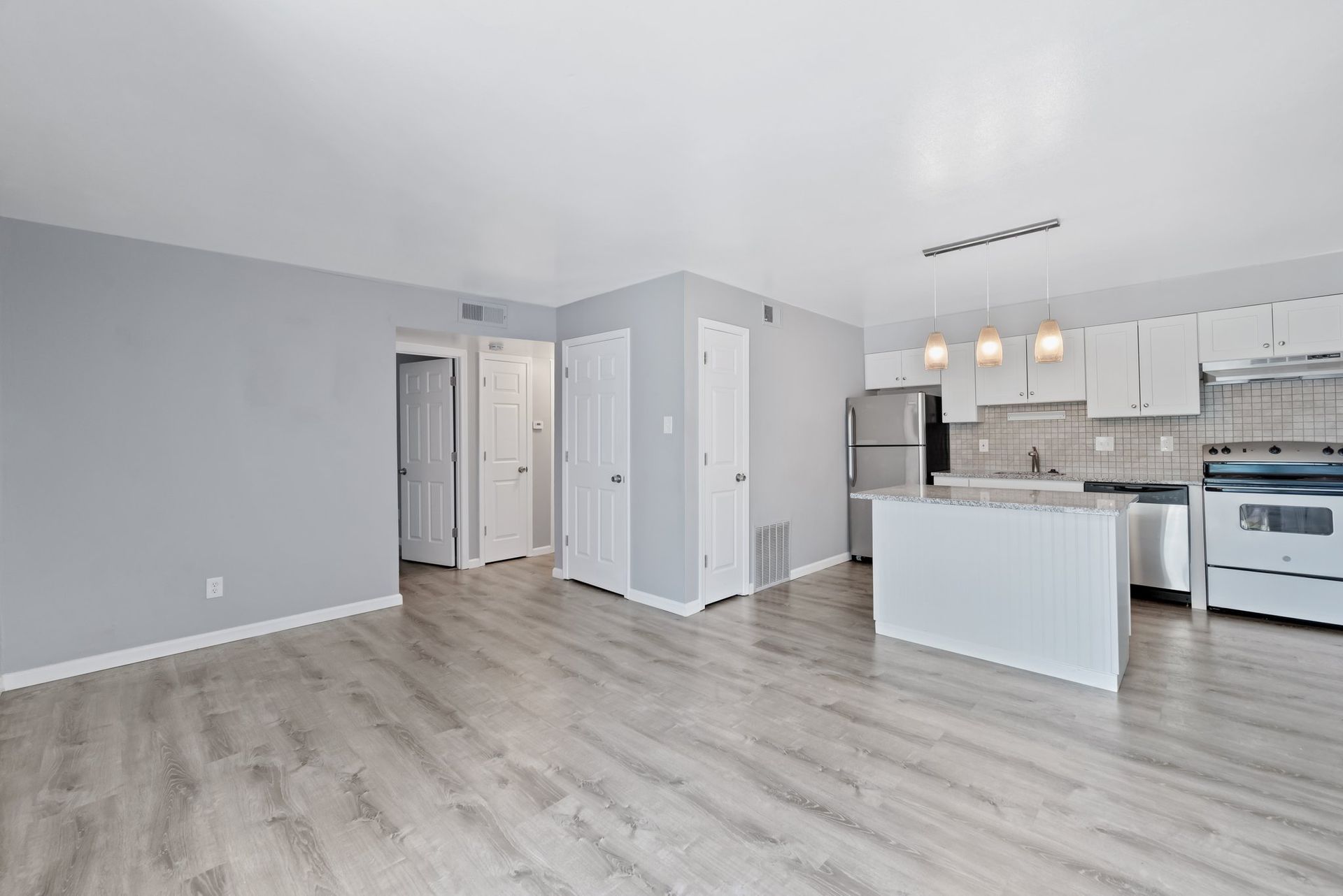 A living room with hardwood floors and a kitchen with white cabinets.