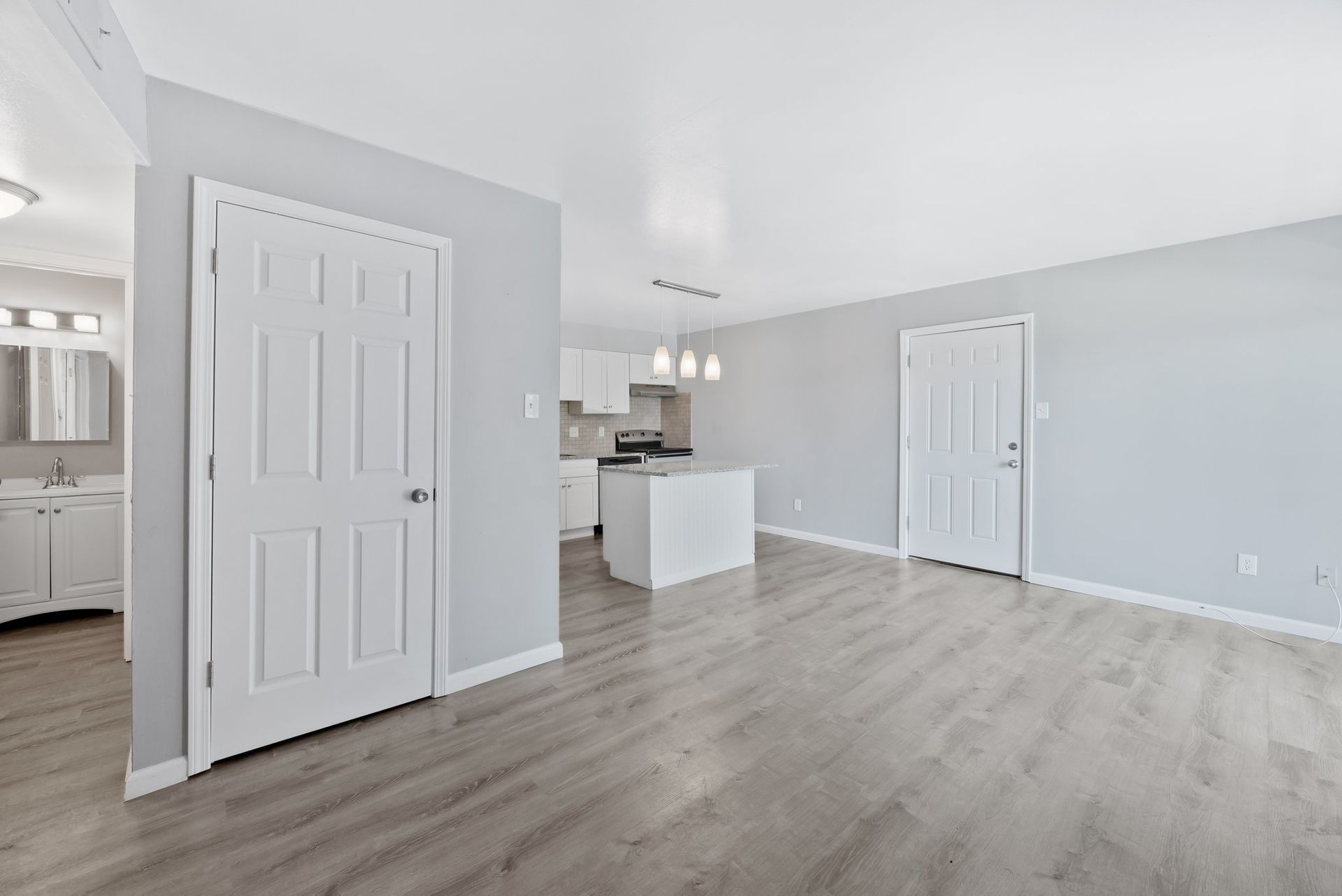 A living room with hardwood floors and a kitchen in the background.
