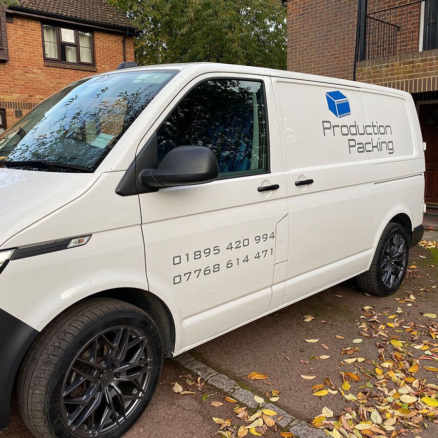 A white van is parked in front of a brick building with the Production Packaging logo on its side