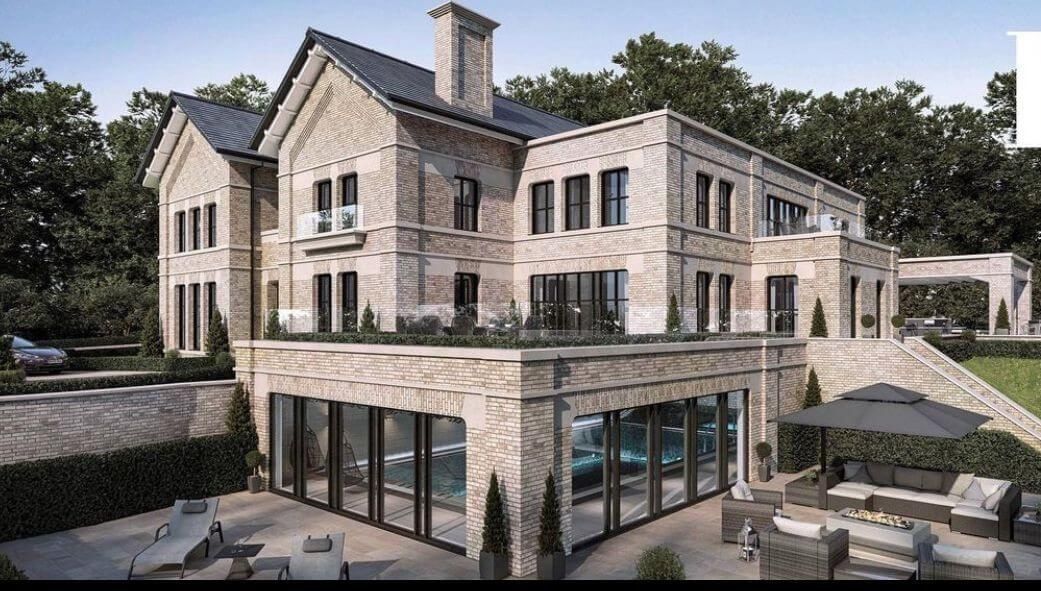 Large stone mansion with glass-walled pool area, patio with seating, and surrounding greenery.