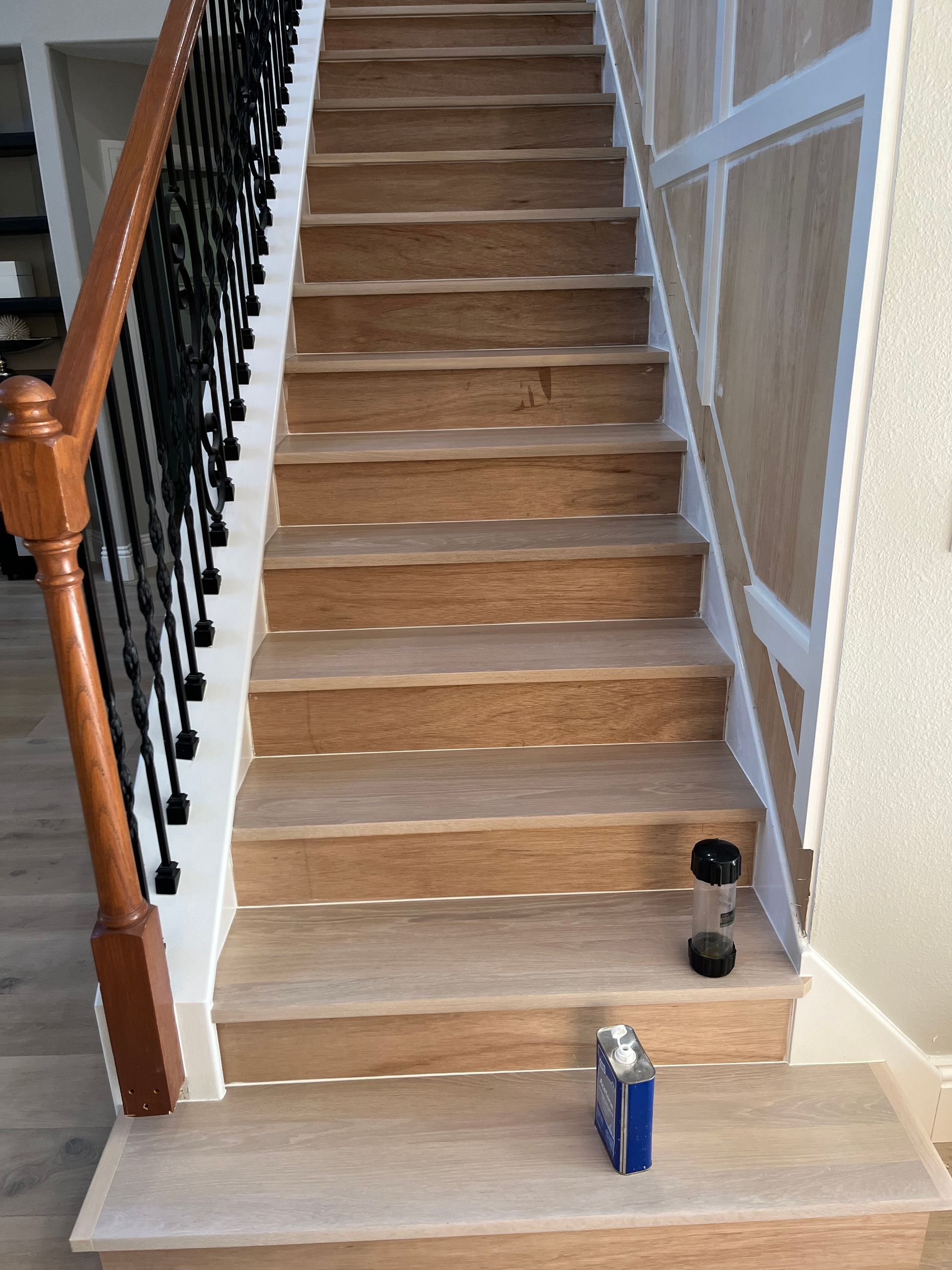 Staircase with light wood steps, dark railing, and white trim. A bottle and a can are on the step.