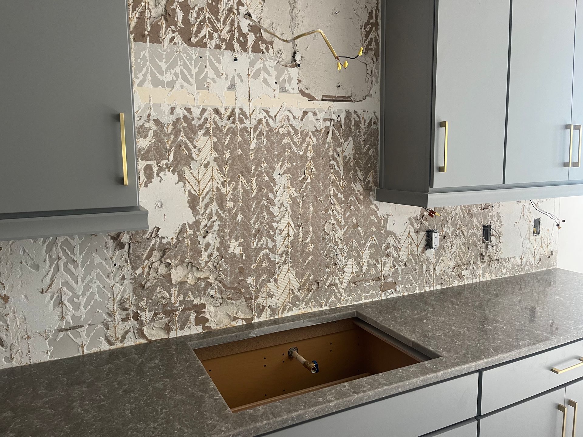 Kitchen backsplash with wallpaper partially removed, gray cabinets and countertop.