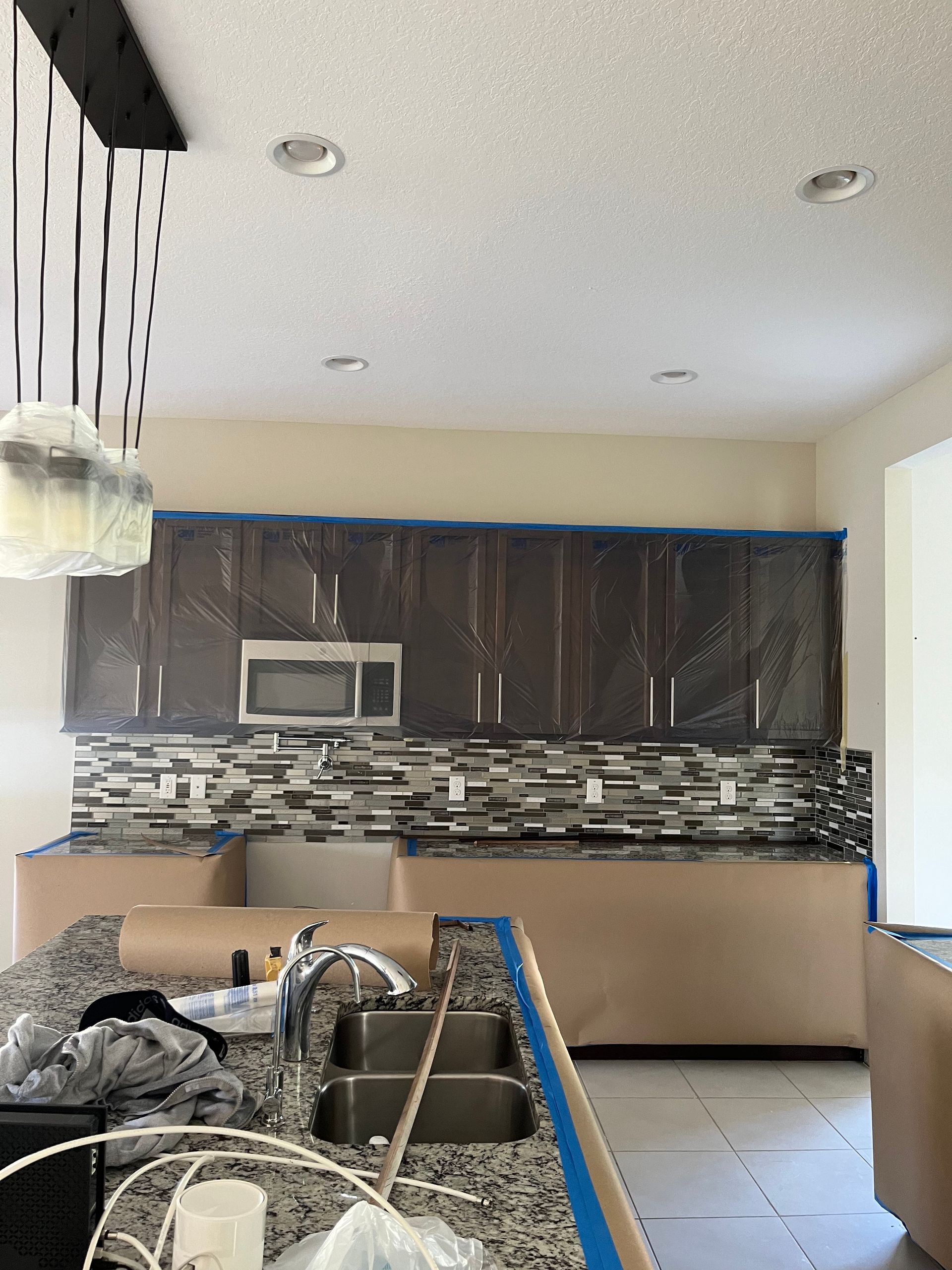 Kitchen under renovation with covered cabinets, backsplash, and island countertop.