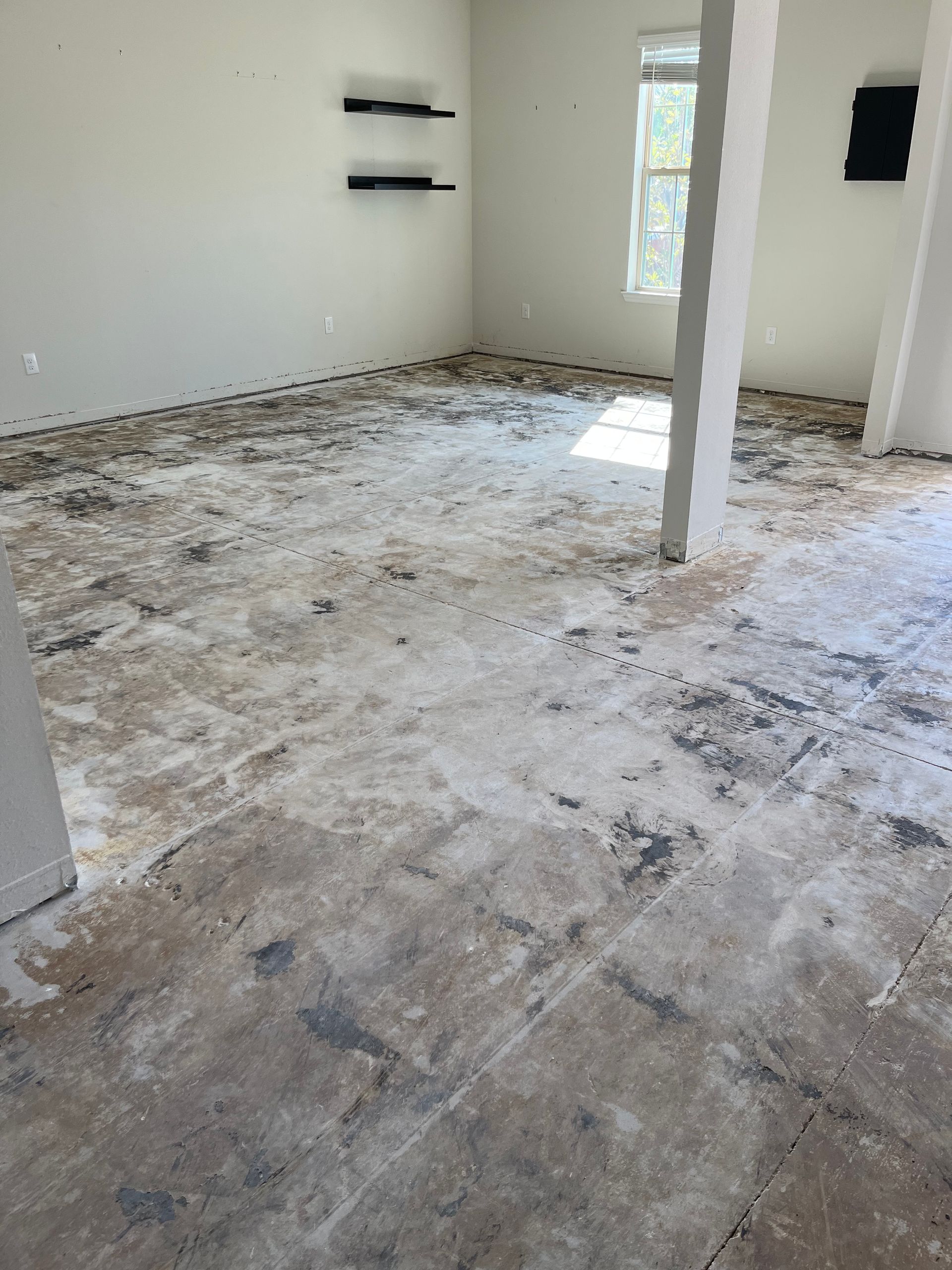 Bare floor with construction debris in an empty room; white walls, natural light.