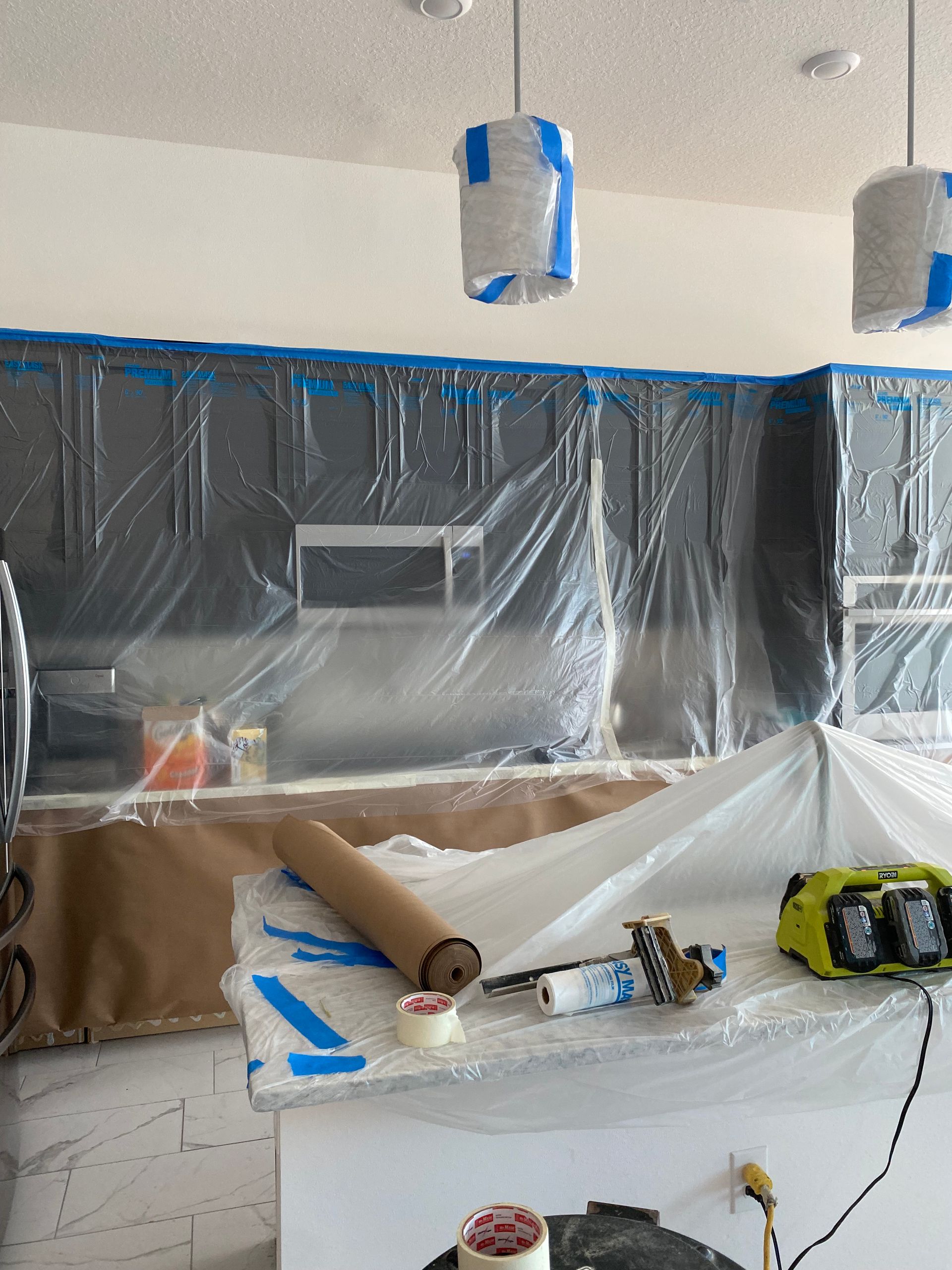 Kitchen cabinets and countertops covered in plastic and tape for painting or renovation.