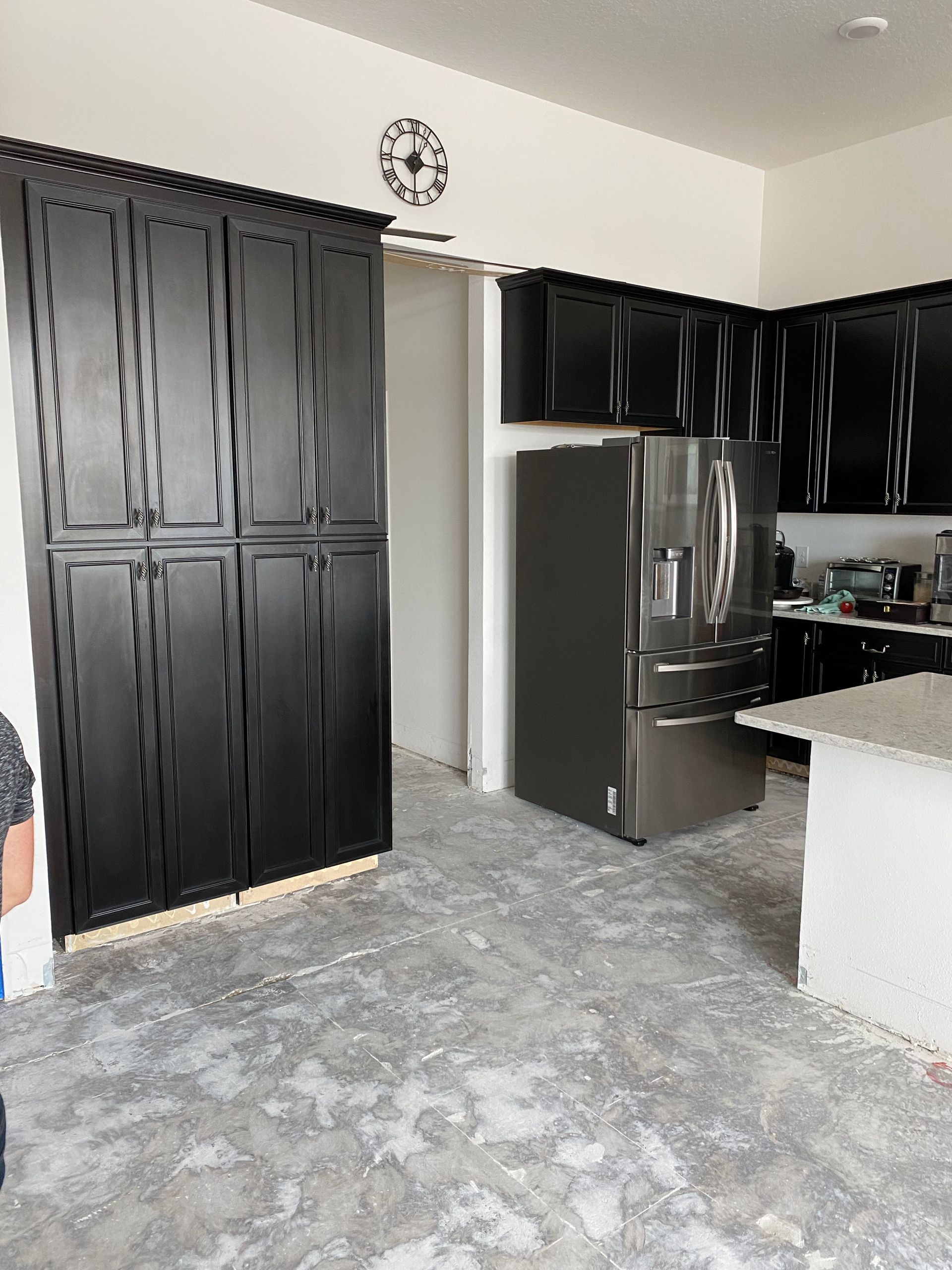 Kitchen with black cabinets, stainless steel refrigerator, and concrete floor.