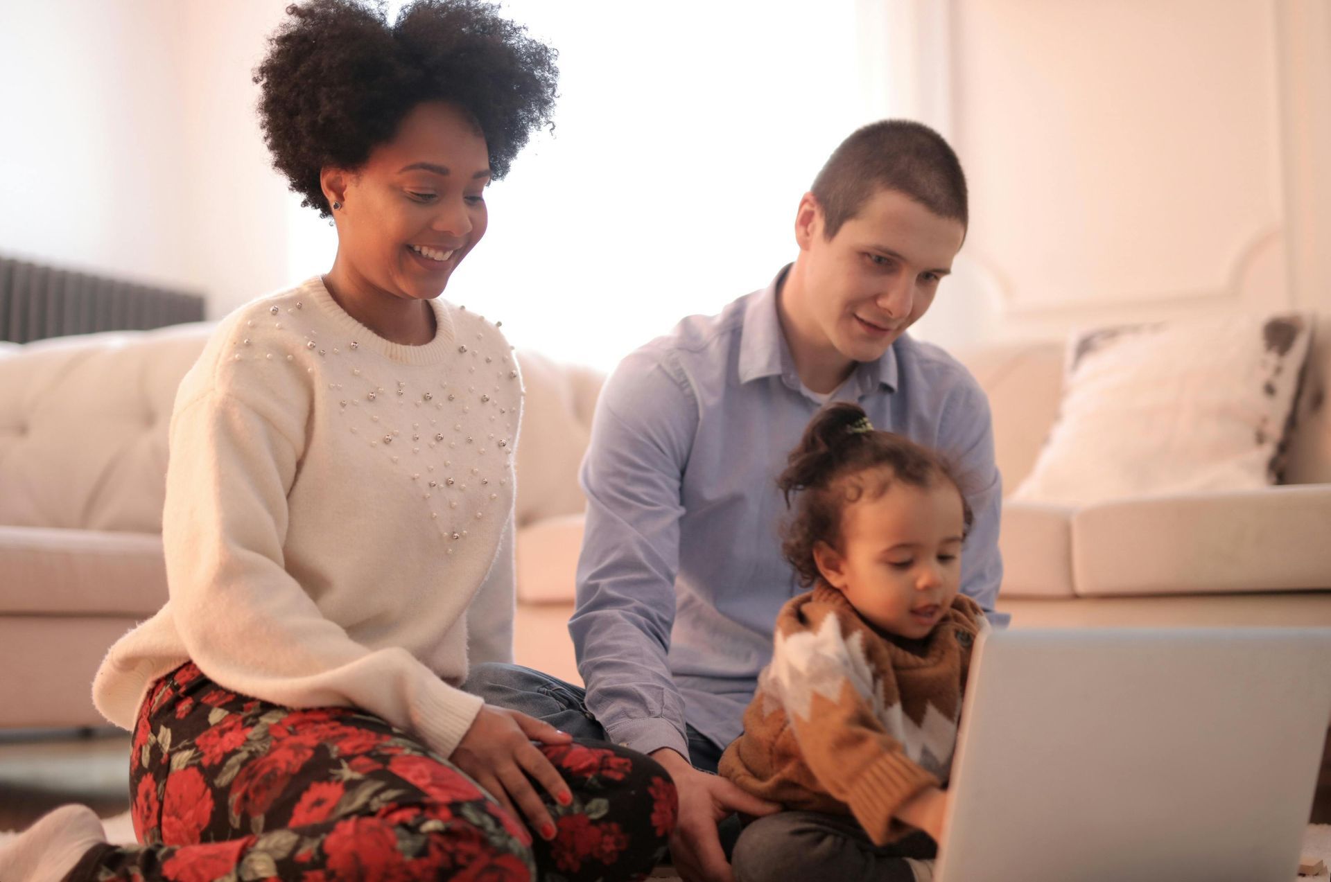 A family is sitting on the floor looking at a laptop computer.