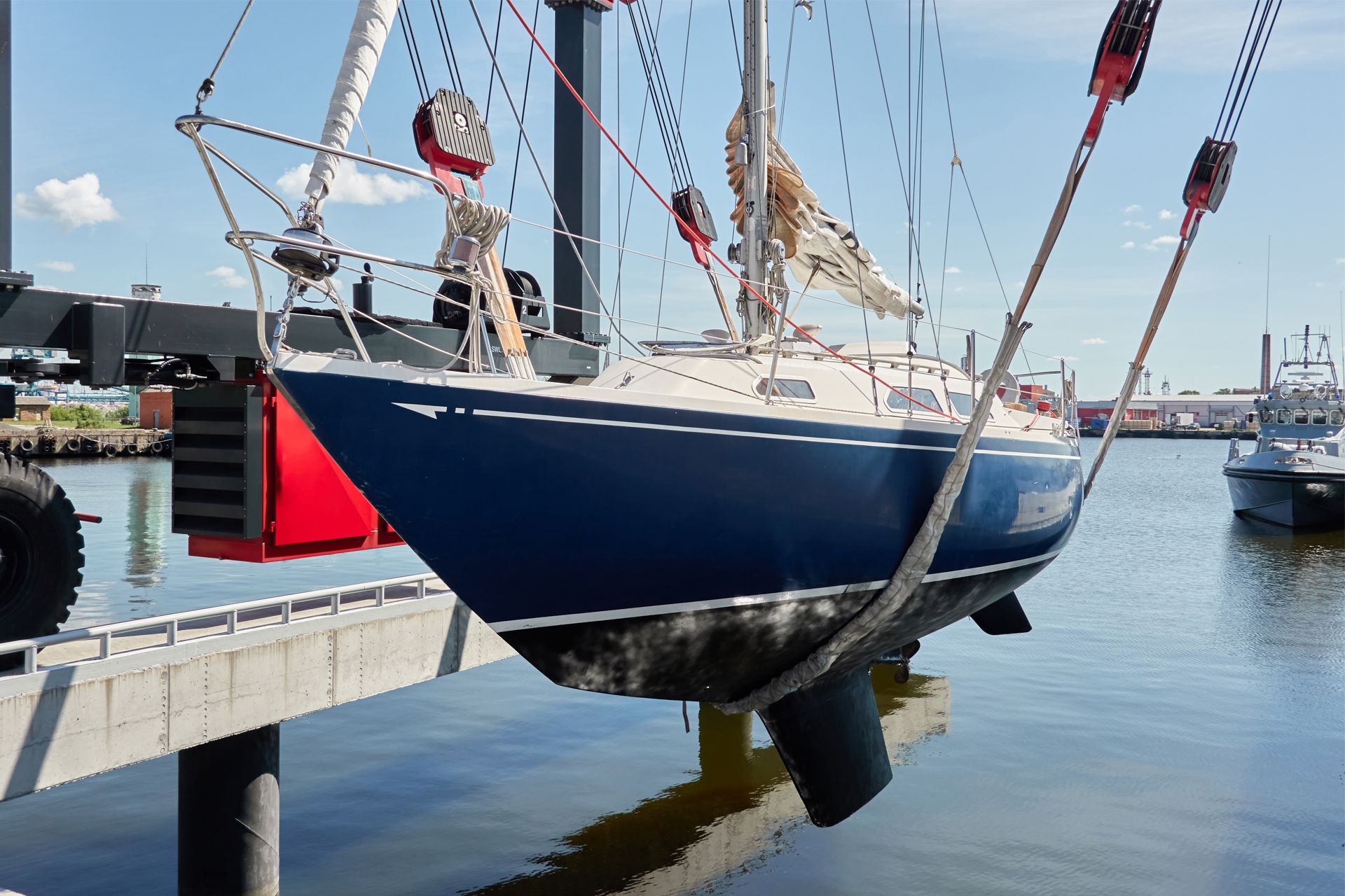A blue sailboat being lifted out of the water by a crane at a marina
