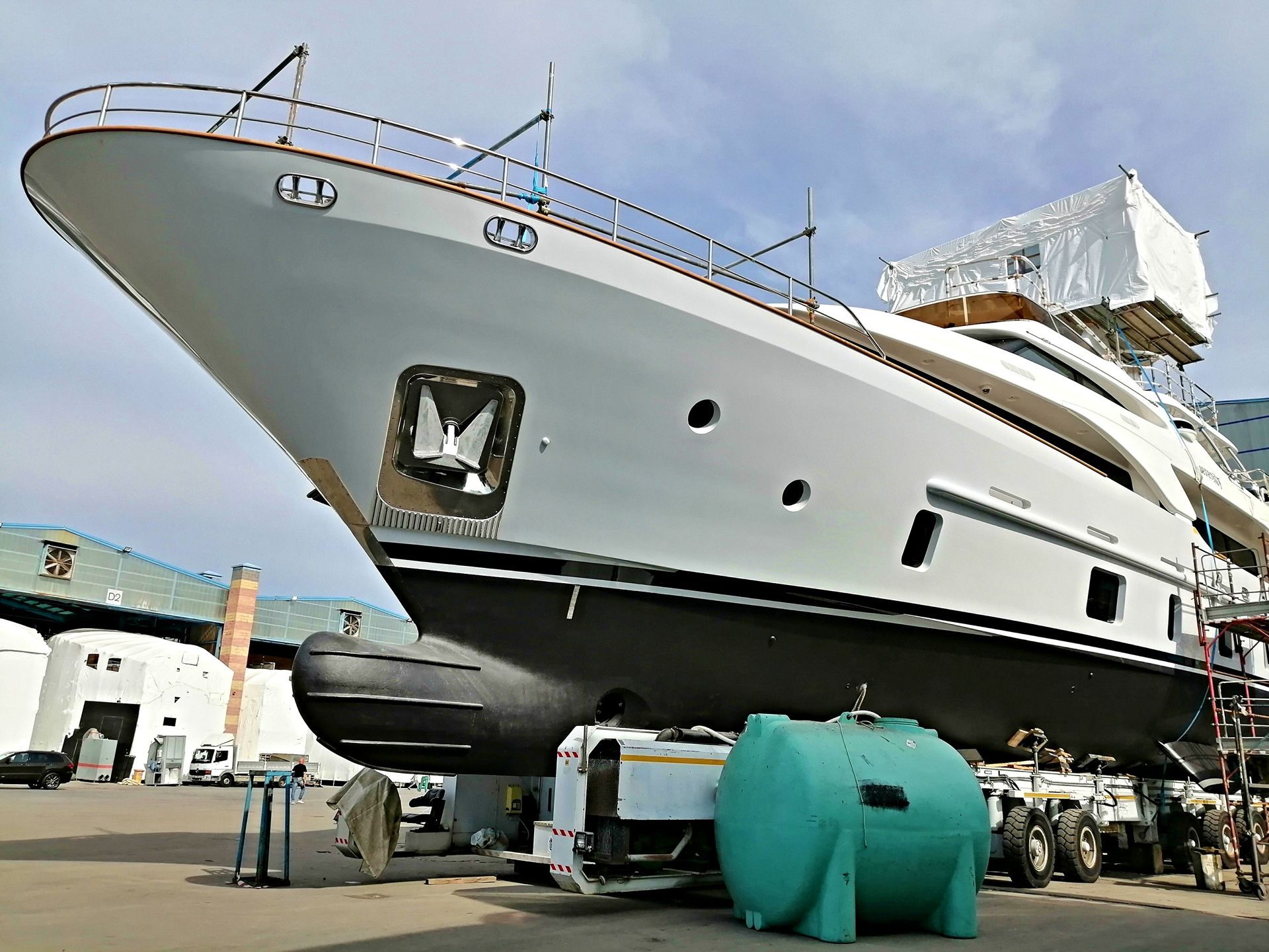 A large white yacht on a trailer in a shipyard