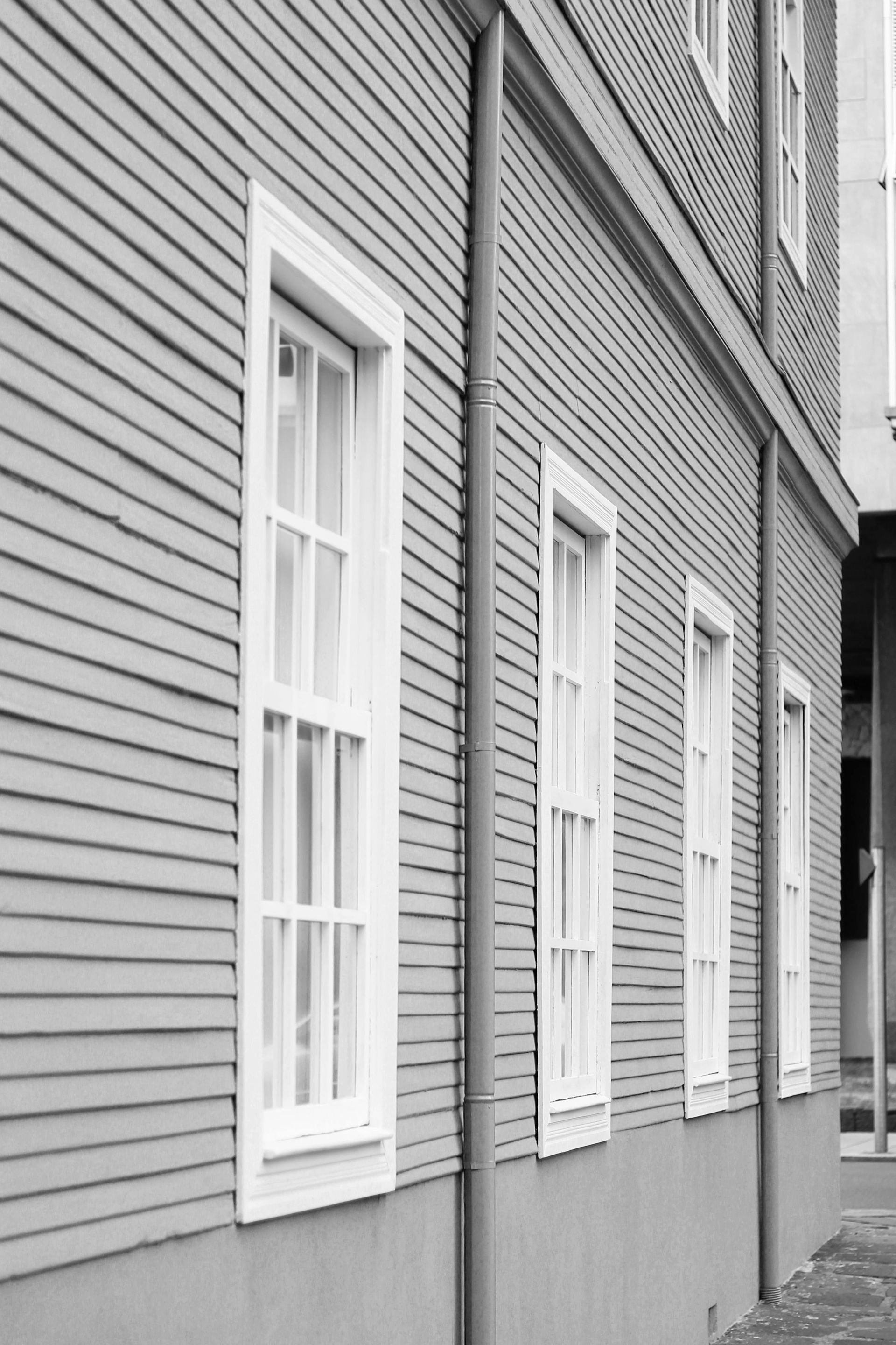 Gray wooden building facade with white-trimmed windows and horizontal siding along a narrow alley.