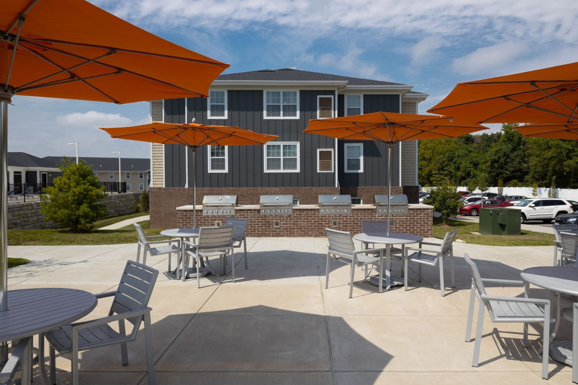 Outdoor community grilling area with orange umbrellas and metal tables in front of a multi-unit building.