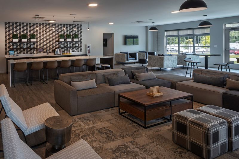 Lounge area with modular sofas, a bar with stools, and several seating areas. Neutral tones, modern design.