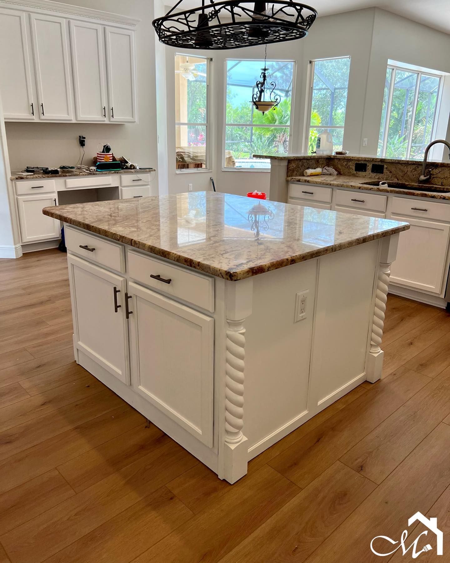Kitchen island with granite countertop, white cabinets, hardwood floors, and a chandelier.