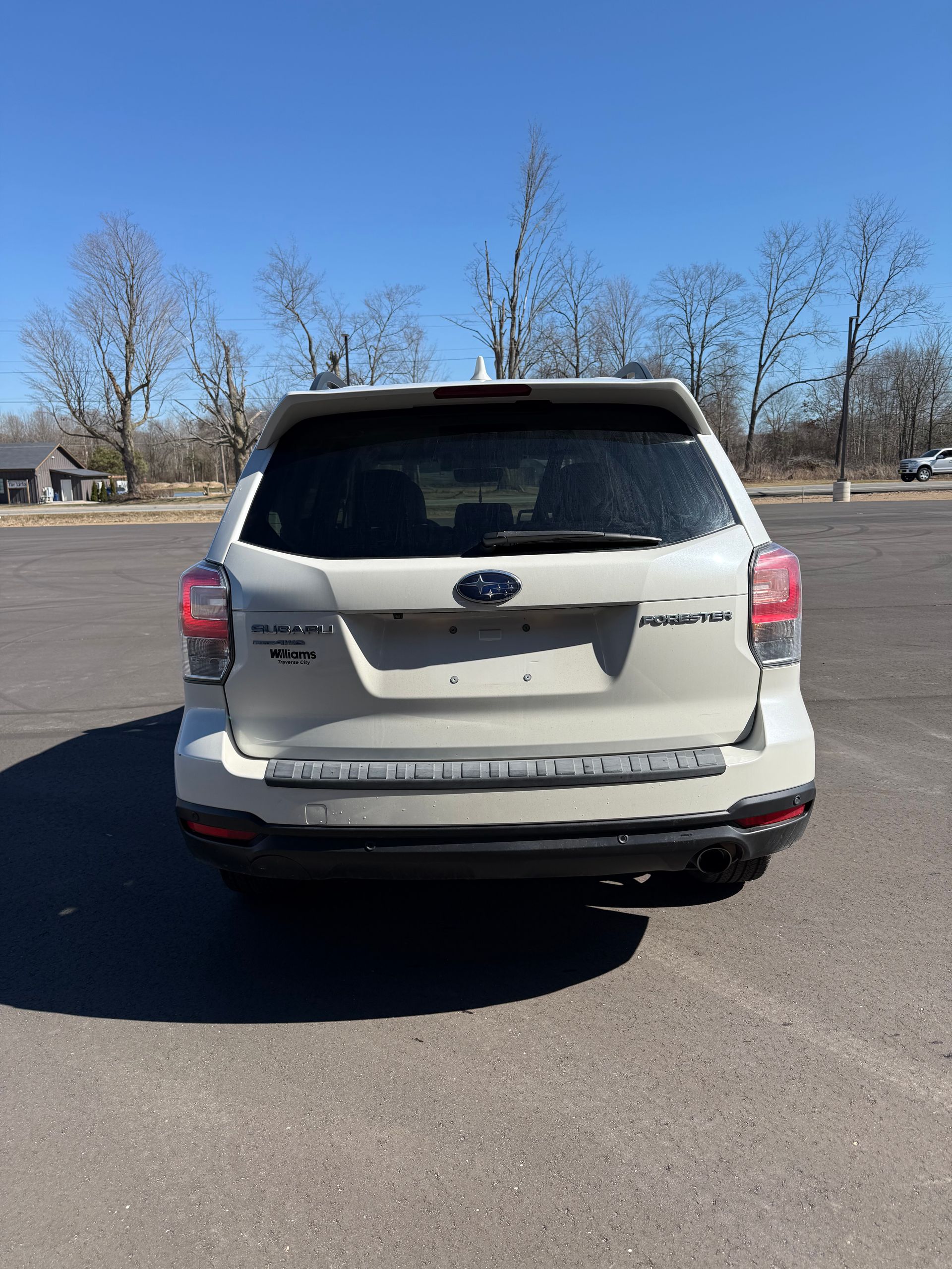 A white Subaru Forester SUV parked in a paved lot under a clear blue sky.