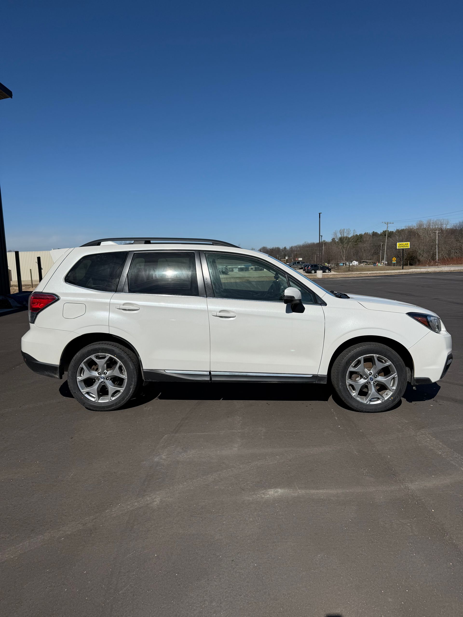 A white Subaru Forester SUV parked in a paved lot under a clear blue sky.