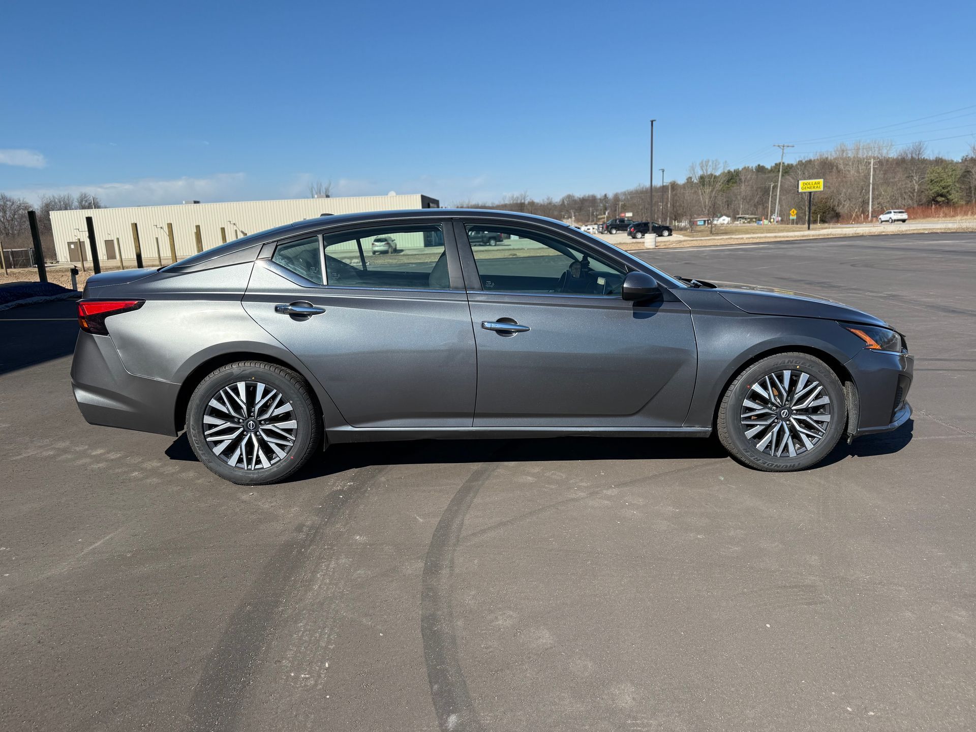 A gray Nissan Altima parked on an asphalt lot in front of a dark, industrial-style building under a clear blue sky.