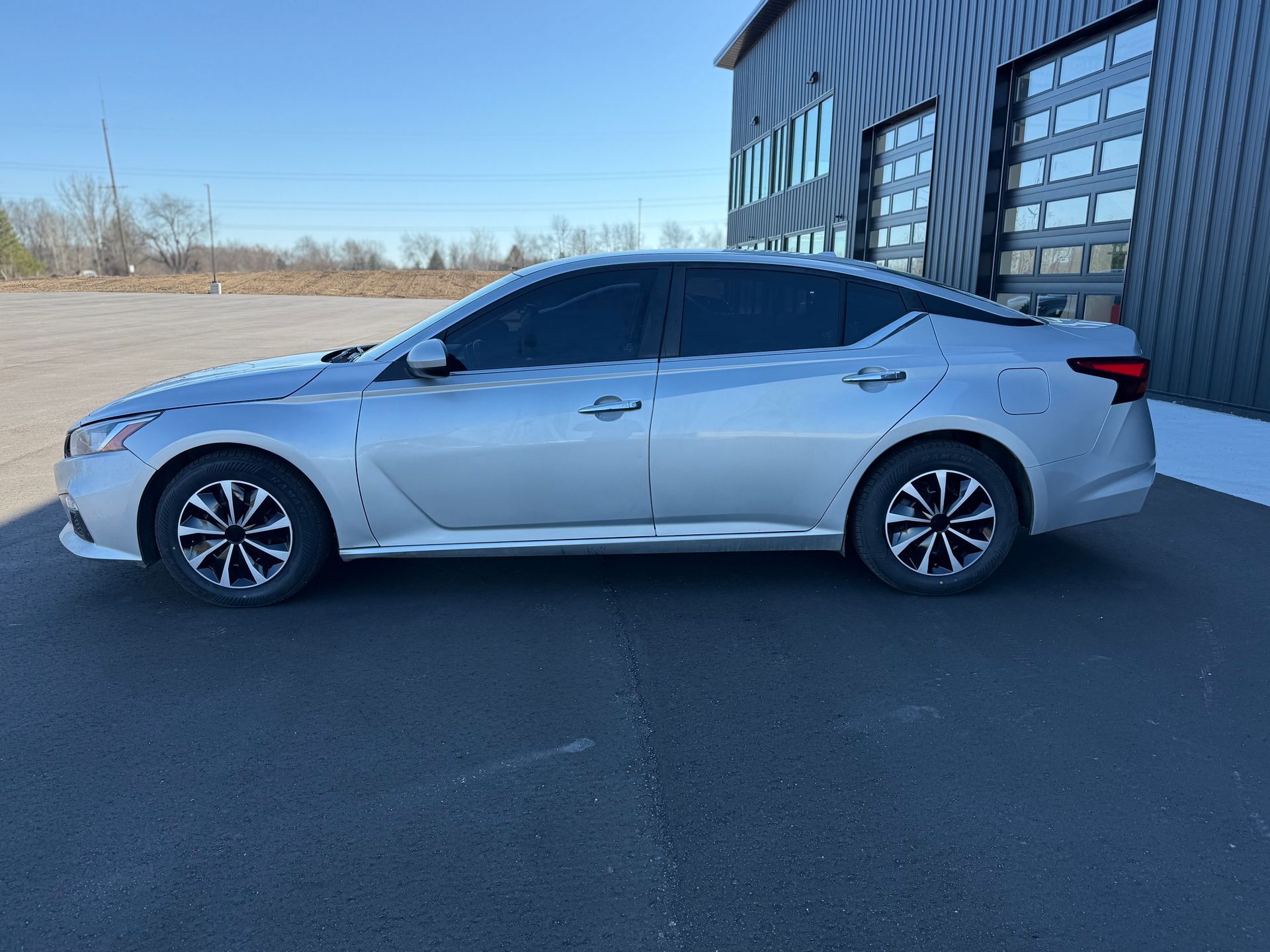 A silver Nissan Altima parked in front of a dark gray modern industrial building.