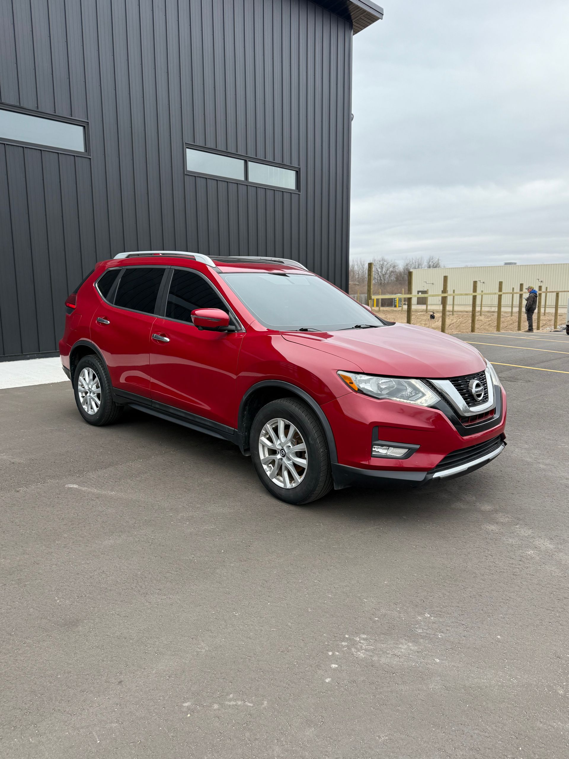 A red Nissan Rogue SUV parked on an asphalt lot in front of a black metal building.