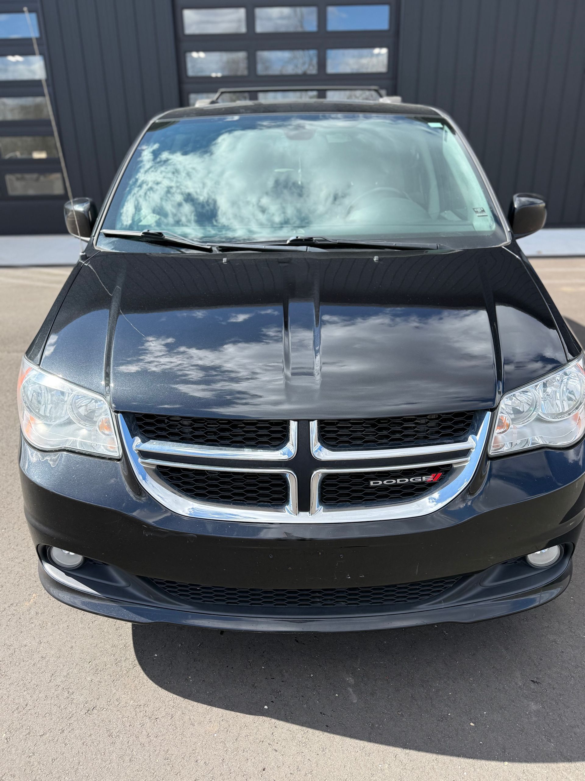 A black Dodge Grand Caravan parked in front of a modern building with large glass garage doors.