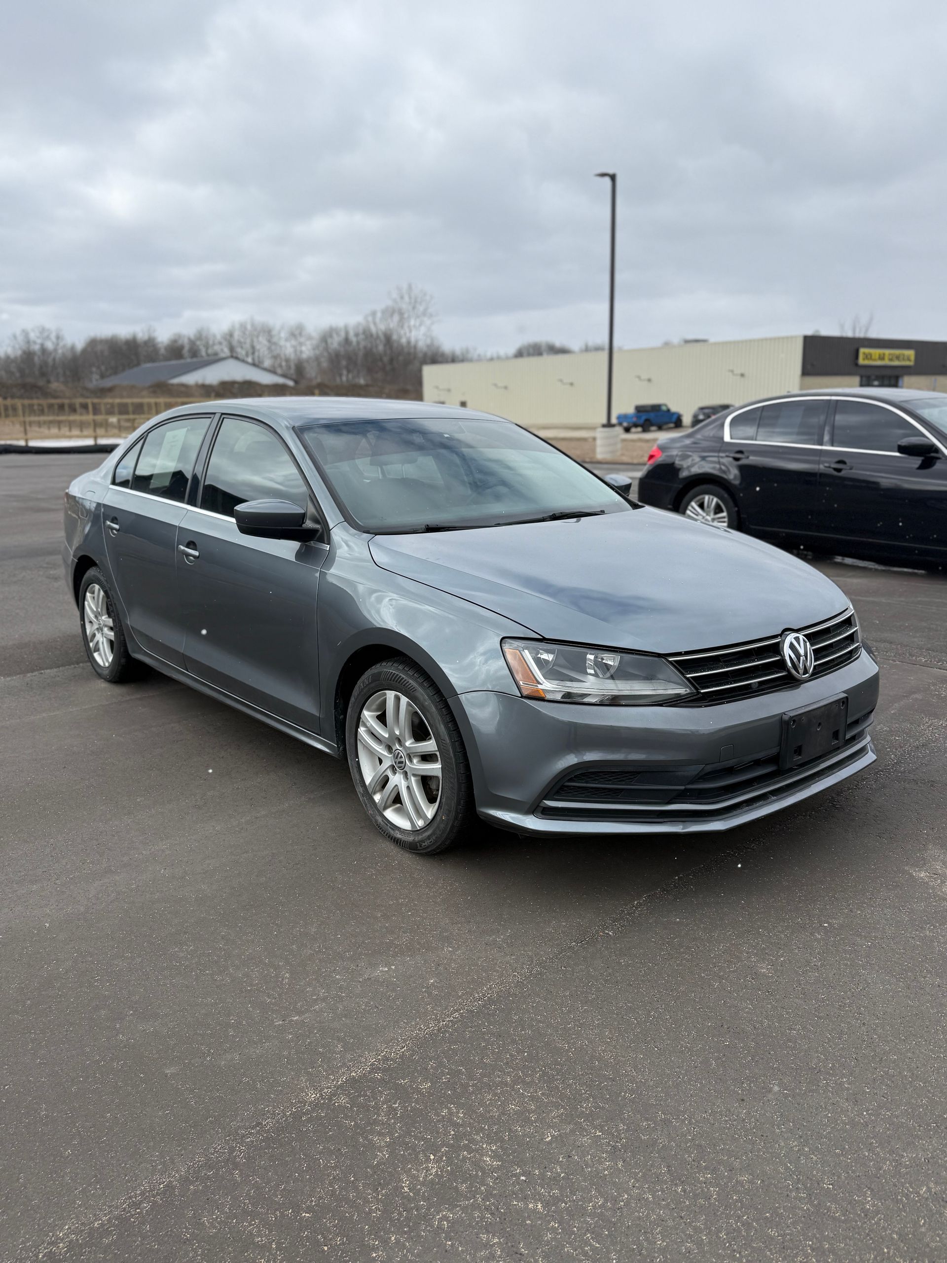 A grey Volkswagen Jetta sedan parked in an outdoor parking lot under a cloudy sky.