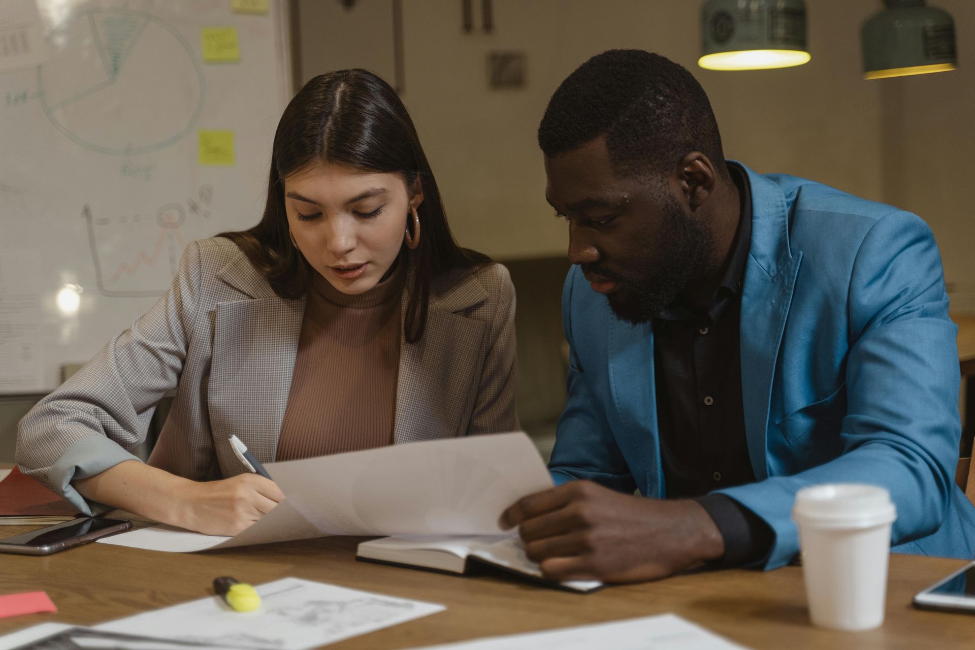 Woman and man reviewing documents at a wooden table in an office setting.