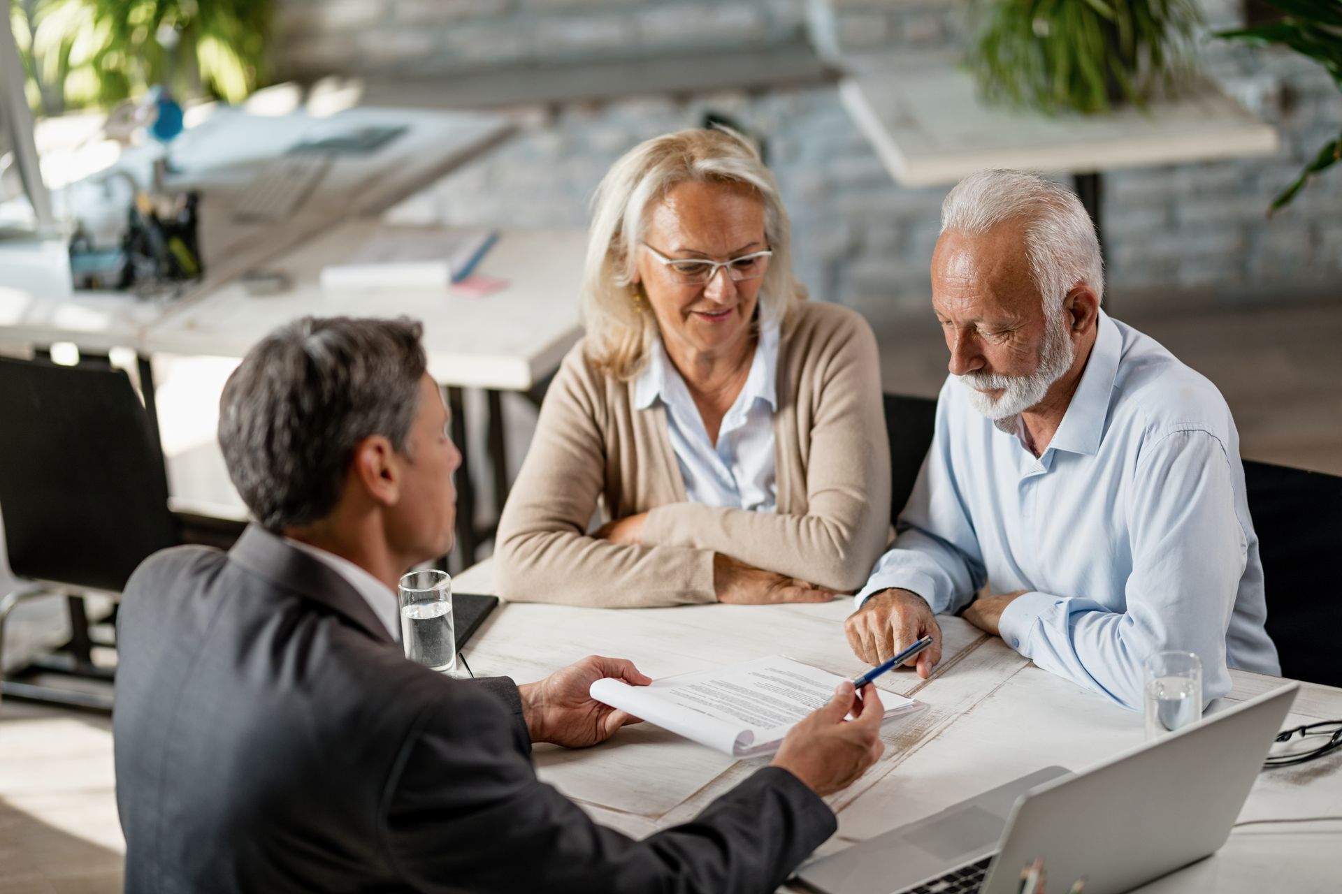 A financial advisor reviews documents with an elderly couple at a desk in an office.