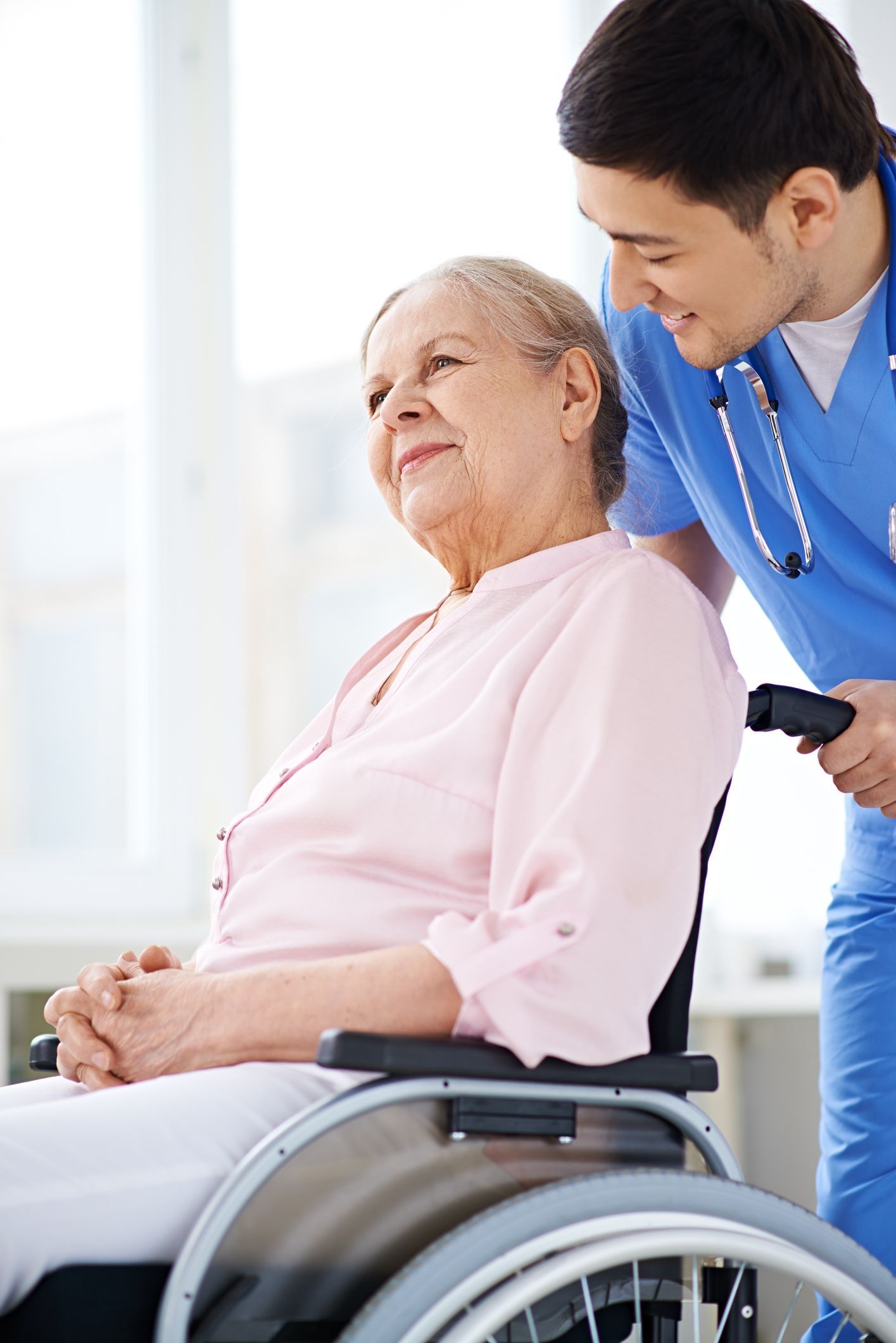 A nurse pushing an old person in a wheelchair during Assisted Living Facility