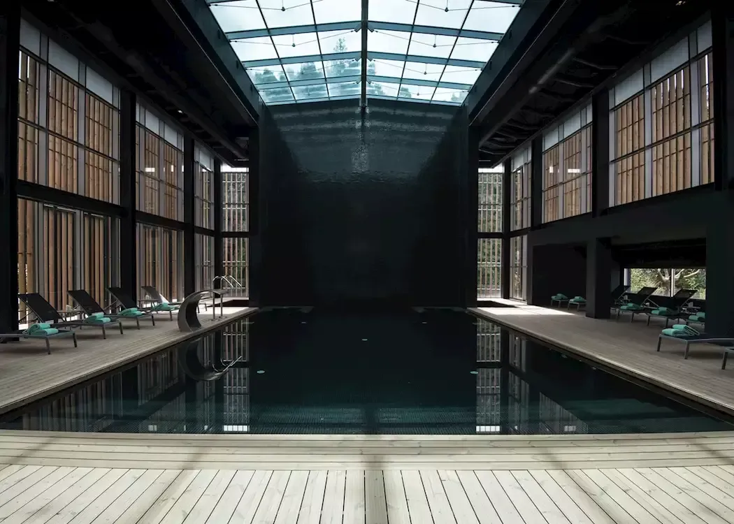 A dark, modern indoor swimming pool with a glass ceiling and surrounding lounge chairs.