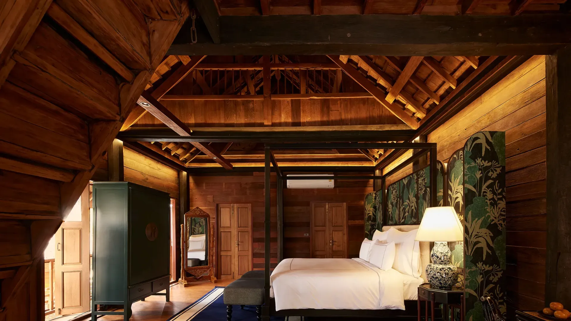 A rustic, dark-wood bedroom with vaulted ceilings, a four-poster bed, green cabinet, and warm, ambient lighting.