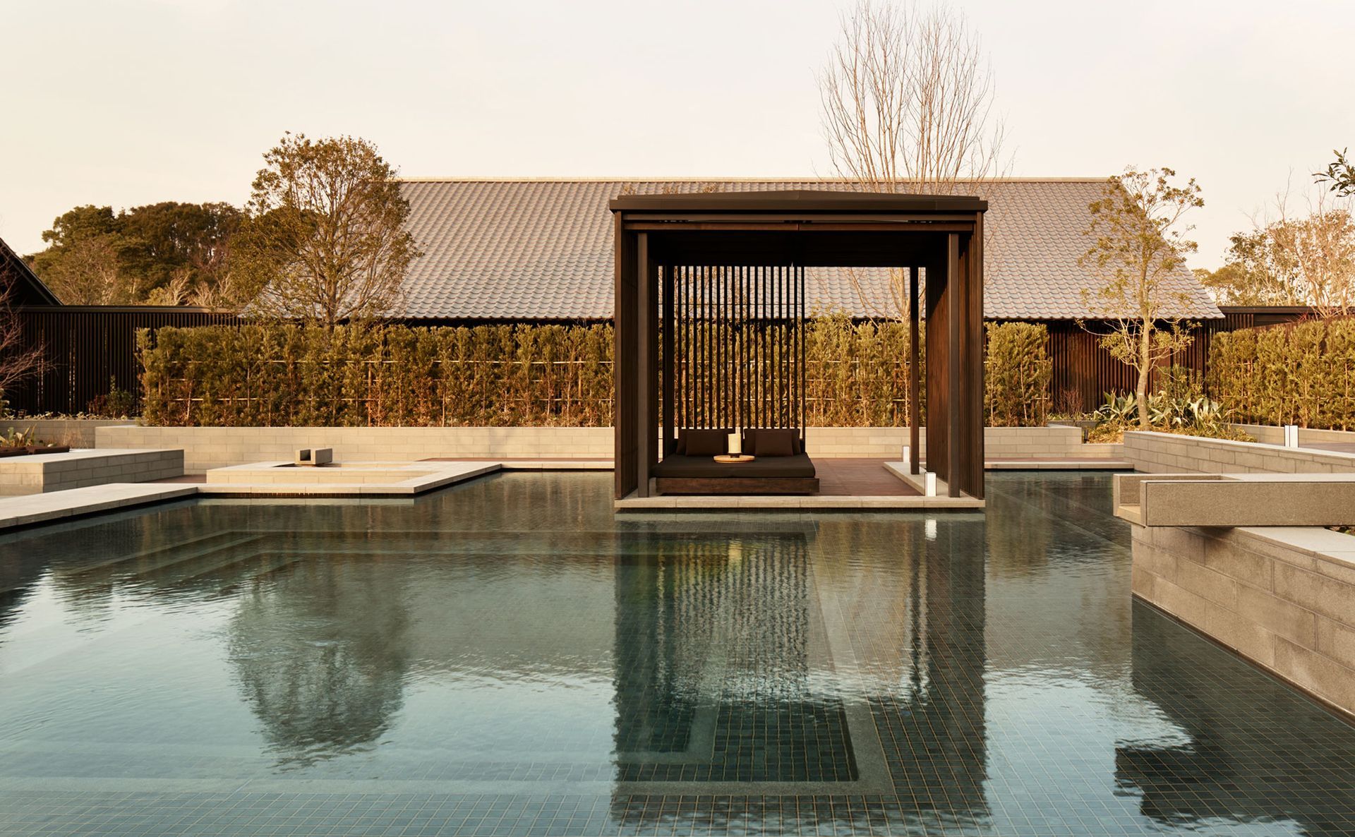 Amanemu, Mie Prefecture A dark wood cabana with cushions floats on a still pool, reflecting the structure and the sky.